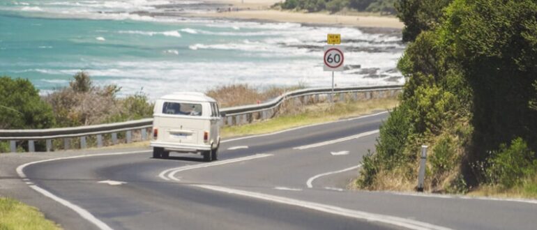 A white van driving on a road next to a sea side