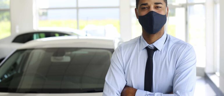 Man standing crossed arms wearing mask in a car dealership