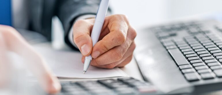 A person holding a pen and writing on a notepad