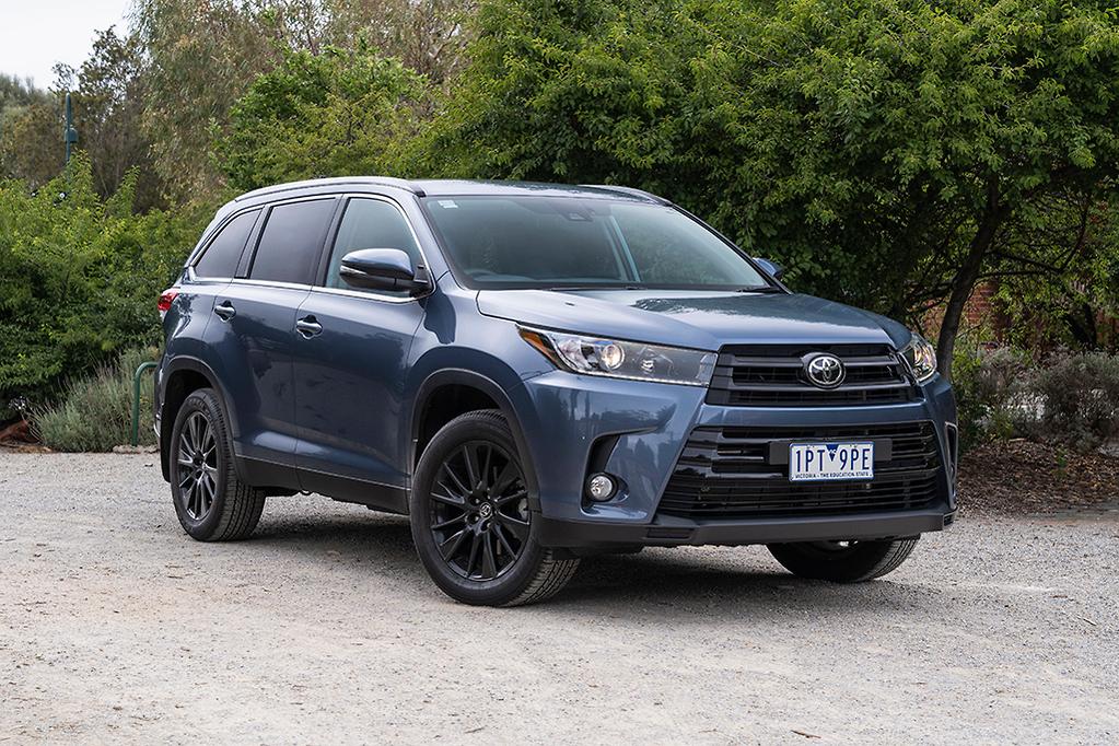dark blue toyota kluger parked on gravel against green trees