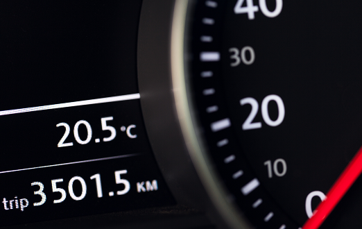 close-up of a car speedometer glowing white, displaying kilometres per hour on a dark dashboard