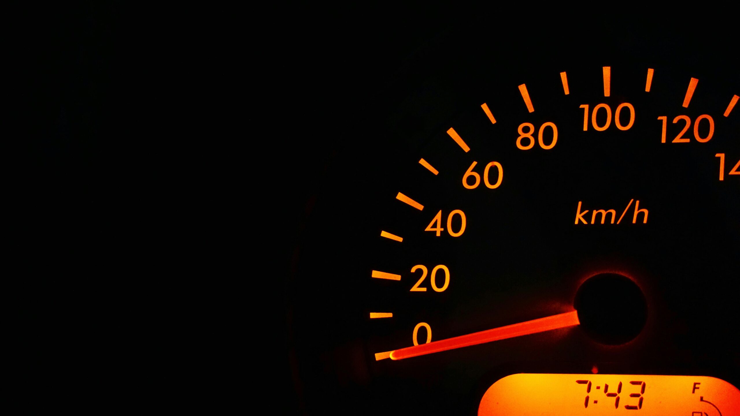 close-up of a car speedometer glowing orange, displaying kilometres per hour on a dark dashboard.