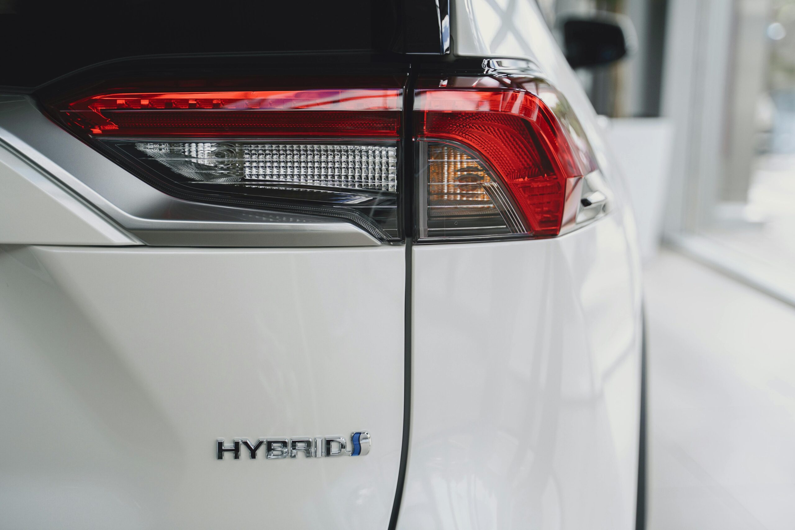 close-up of the rear taillight and chrome "HYBRID" badge on a white Toyota RAV4 in a showroom.