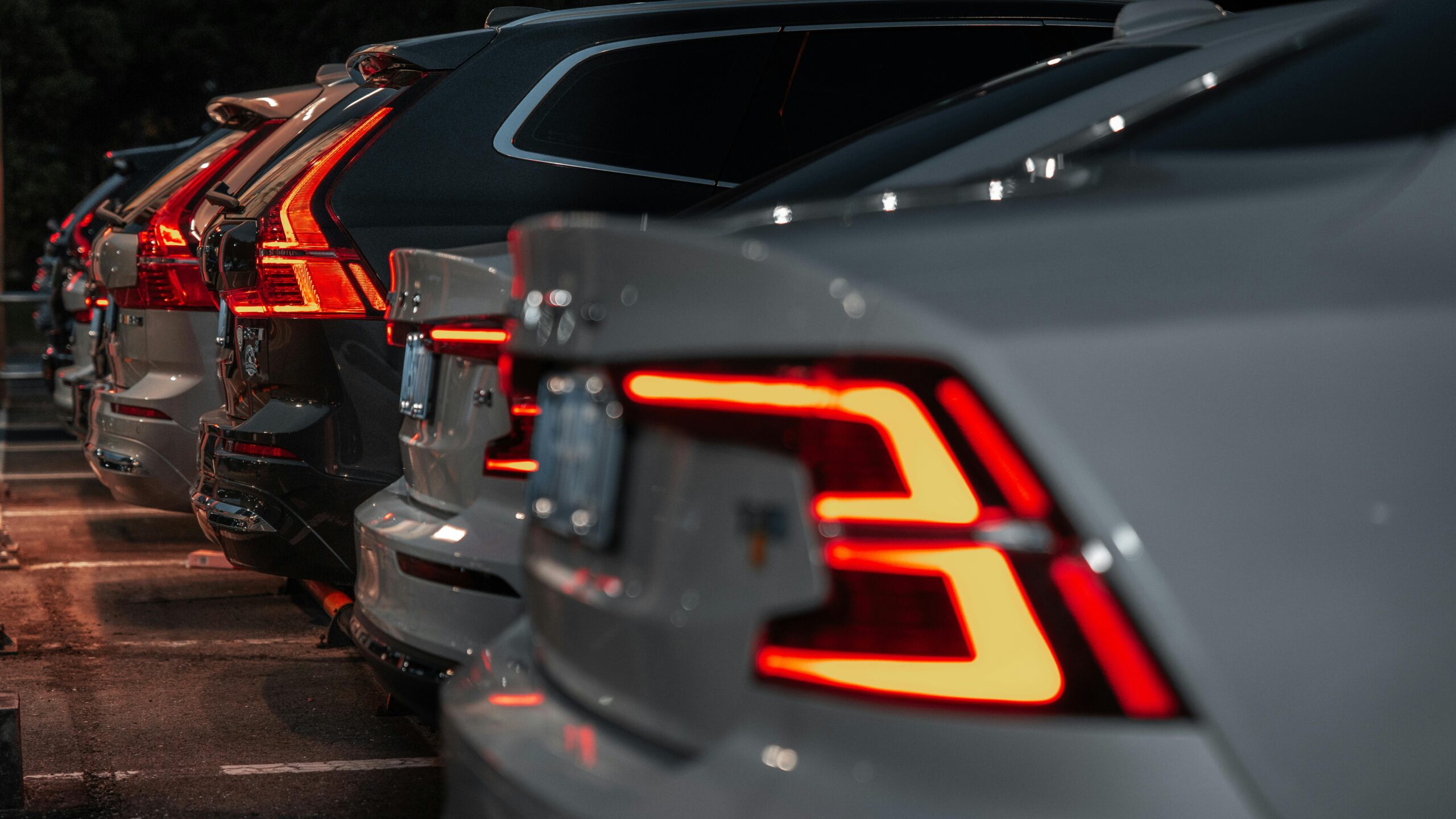 row of parked Volvo cars at night, focusing on their glowing red led signature taillights