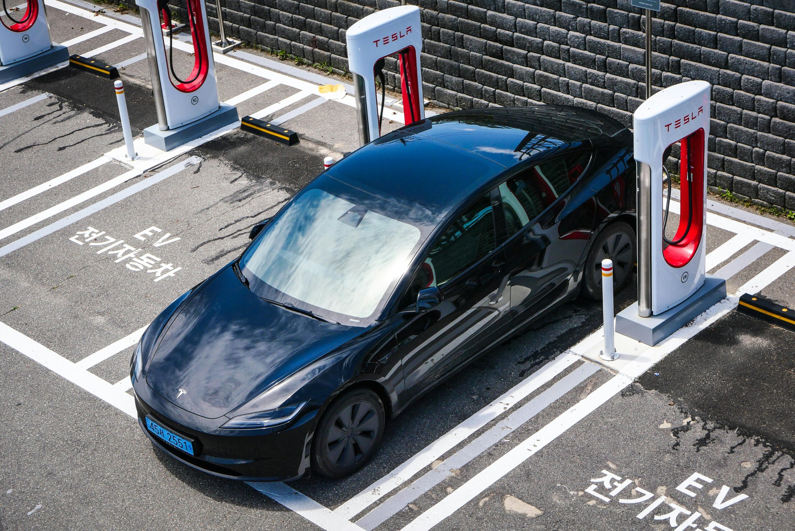 A black Tesla parked at a charging station in an urban setting